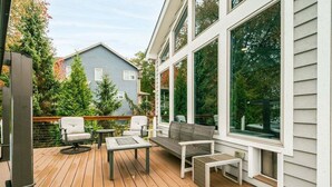 A wooden deck with outdoor furniture, large windows, and a view of a neighboring house.