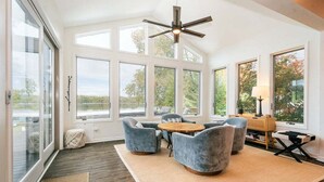A spacious room with large windows, a ceiling fan, and a round wooden table surrounded by chairs.