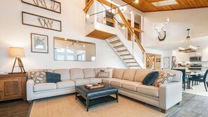 A modern living room with a sectional sofa, a coffee table, a staircase, and a kitchen in the background.