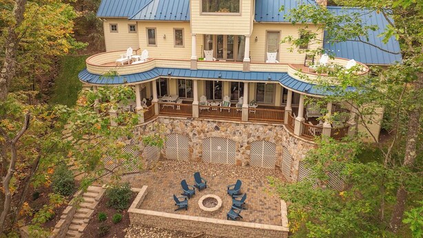 A large house with a blue roof, a covered patio with outdoor furniture, and a stone fire pit.