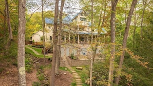 A house surrounded by trees with a stone pathway leading to a wooden bridge.