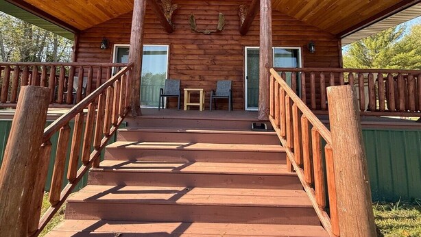 Une cabane en bois avec un porche couvert, deux chaises et une table.