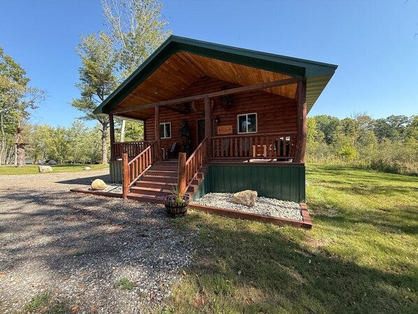 A wooden cabin with a porch, a staircase, and a gravel driveway.