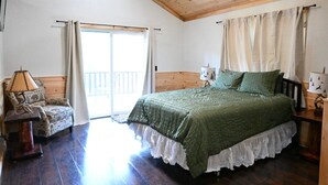 Une chambre avec un plafond en bois, un lit avec une literie verte, une chaise et une table de chevet avec une lampe.