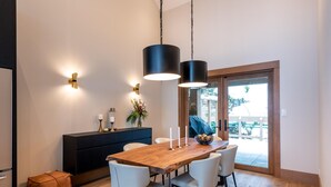 A modern dining area with a wooden table, white chairs, and pendant lighting. - Northern Lights 32 | Ski-in/out Luxury Townhome, Hot Tub, (Whistler)