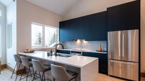 A modern kitchen with dark blue cabinets, a stainless steel refrigerator, and a central island with bar stools. - Northern Lights 32 | Ski-in/out Luxury Townhome, Hot Tub, (Whistler)