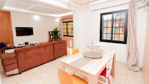 A modern living room with a sofa, dining table, and TV. - Yalie Home and Co (Rivieria 3 bonoumin)