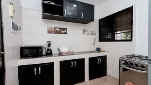 A kitchen with a microwave, coffee maker, and stove. There are black cabinets and a window. - Yalie Home and Co (Rivieria 3 bonoumin)
