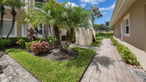 A pathway leading to a building with palm trees and a well-maintained lawn. - Charming Three Bedroom Villa in Beautiful Naples (Naples)