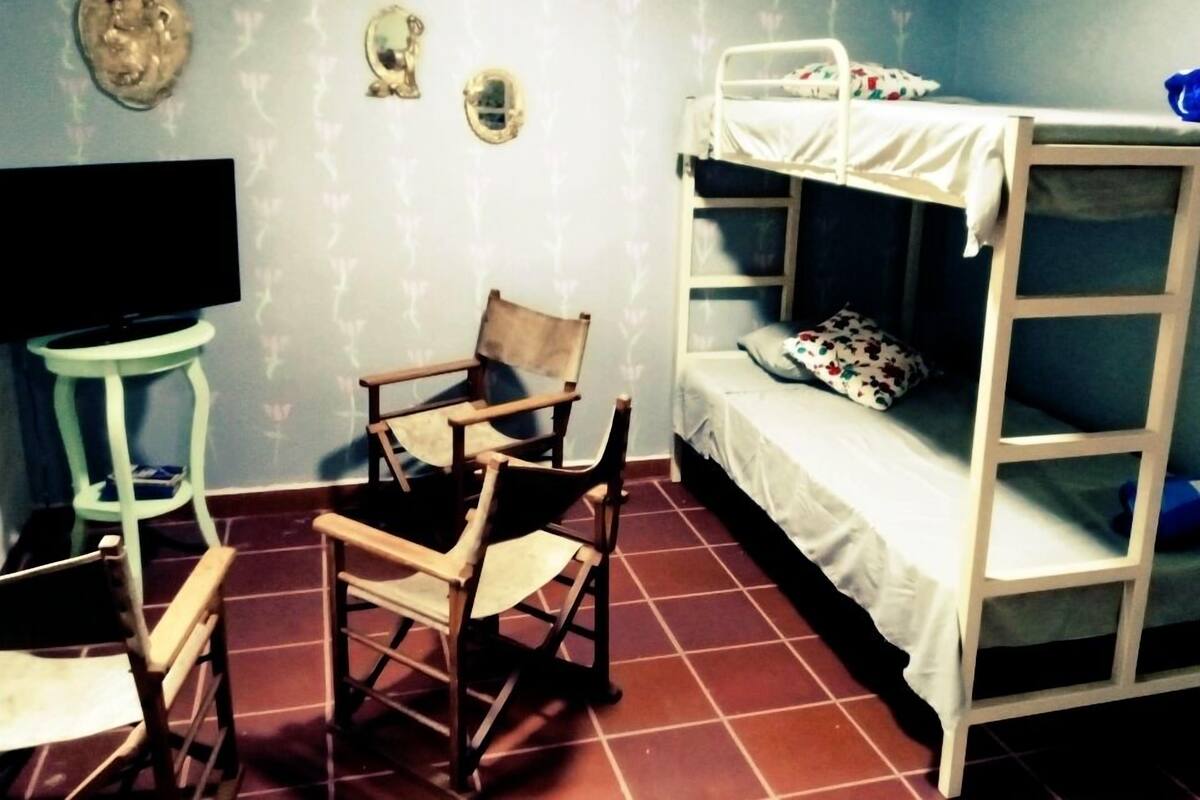 A room with a bunk bed, a wooden chair, a small table, and a television.