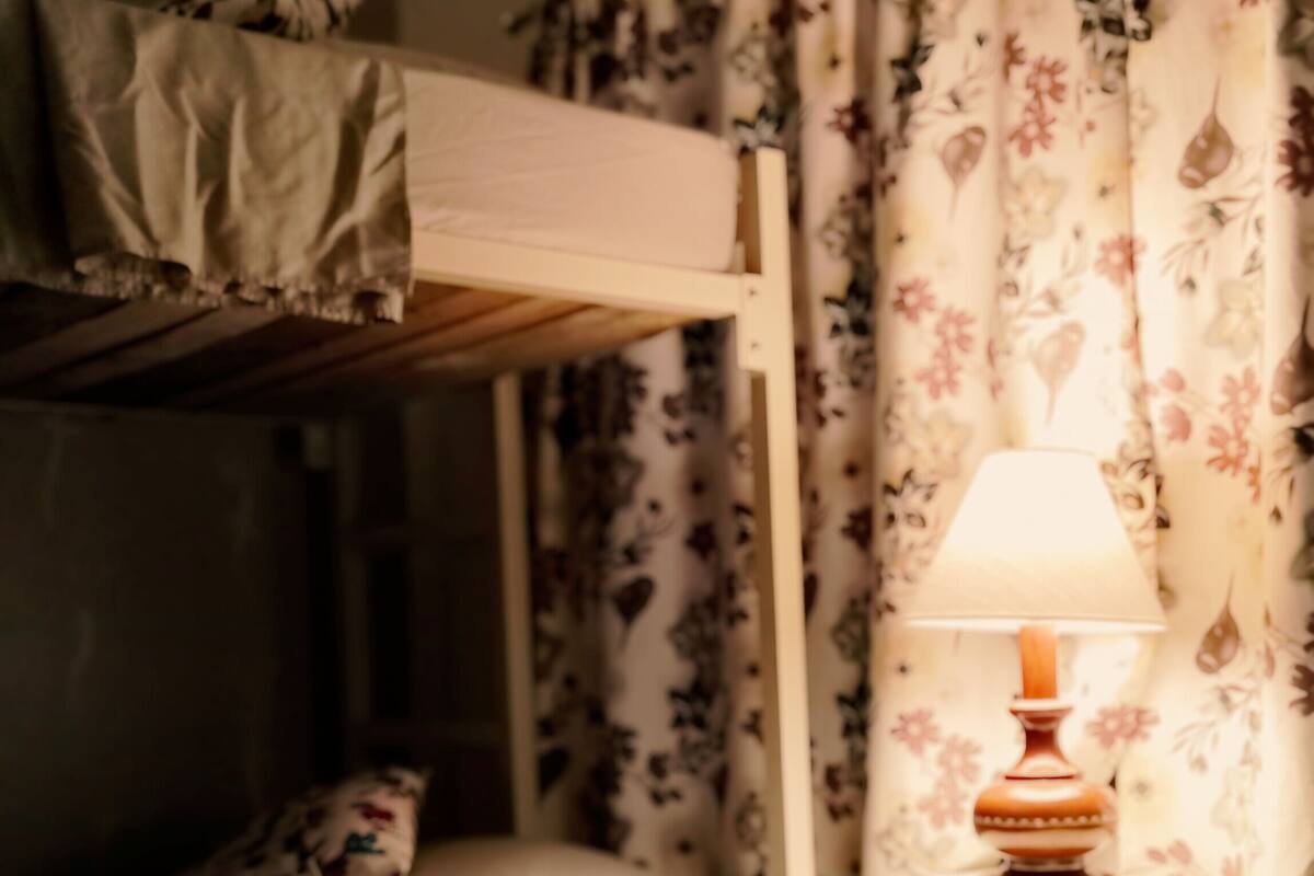 A bunk bed with a bedside table and lamp, a floral curtain, and a green nightstand.