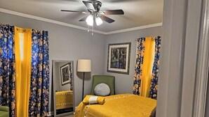 Una habitación de hotel con una cama, ventilador de techo, lámpara y cortinas estampadas.