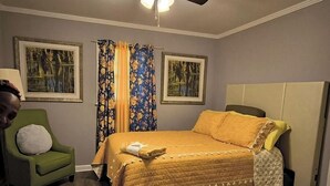 Un dormitorio con una cama, un sillón verde y dos cuadros enmarcados en la pared.