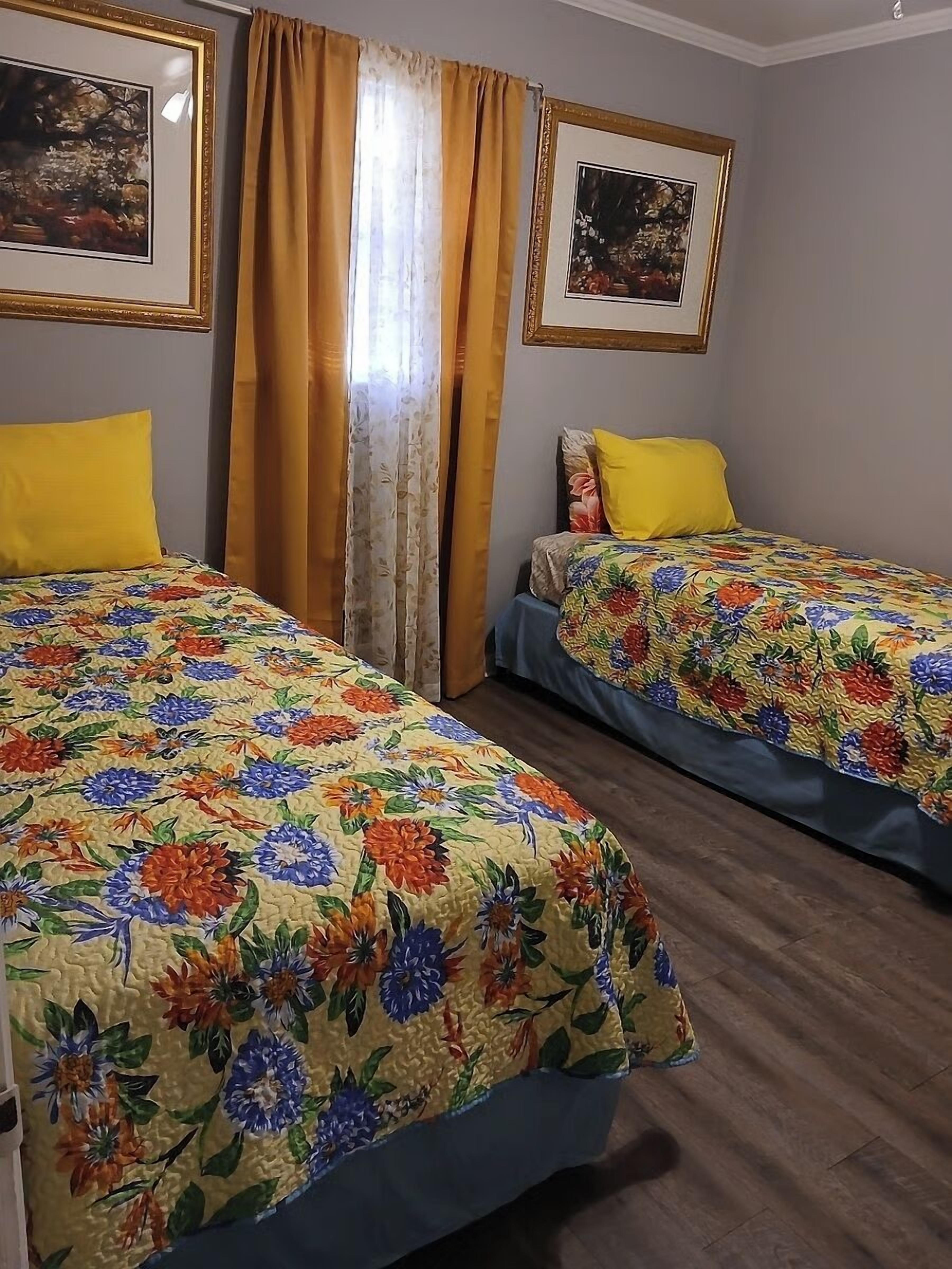 Habitación de hotel con dos camas, cubrecamas estampados y almohadas amarillas, y cuadros en las paredes.