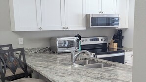 Una cocina con gabinetes blancos, encimera de mármol, tostadora integrada y pileta de acero inoxidable.