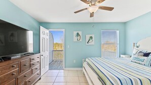 A bedroom with a bed, a dresser, a ceiling fan, and a door leading to an outdoor area. - Full Duplex -Steps to Beach, Dining & Shops, 6 Sunny Balconies, Cozy Firepit! (Gulf Shores)