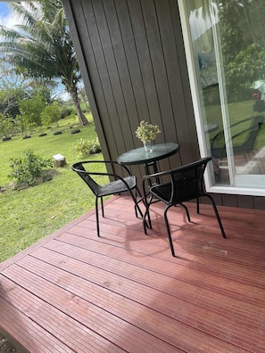 Eine Holzterrasse mit zwei Stühlen und einem Tisch, mit Blick auf einen Garten mit verschiedenen Pflanzen und einer Palme.