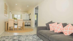 Una sala moderna con un sofá gris, un cojín estampado y un comedor con una mesa y sillas de madera.
