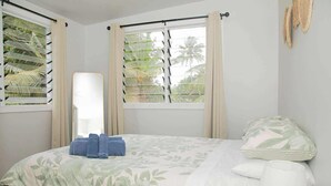 Un dormitorio con cama, ventana con cortinas, mesita de noche y lámpara.