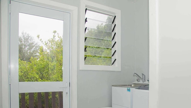 Una sala de lavandería con lavadora, lavadero y ventana con persianas.