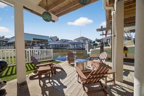A wooden deck with Adirondack chairs, a small round table, and a view of a body of water and buildings in the background.