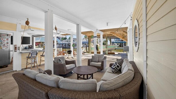 A covered outdoor seating area with wicker furniture, a round table, and a grill.