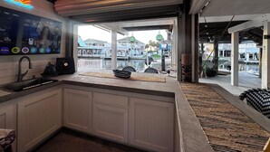 A kitchen with a view of a waterfront, a TV mounted on the wall, and a fan on the counter.