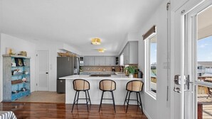 A modern kitchen with a central island, bar stools, and a view through large sliding glass doors.