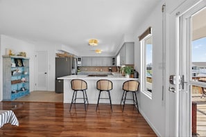 A modern kitchen with a central island, bar stools, and a view through large sliding glass doors. - Canal-Front Fishing & Beach Home -Large Kitchen and Outdoor Spaces - Sleeps 10+ (Galveston)