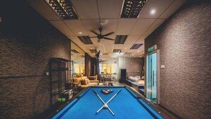 A pool table in a room with a ceiling fan, a sofa, and a glass door leading to another area. - Tun Aminah Shoplot 10-14pax KTV Mahjong Funhouse (Sekudai)