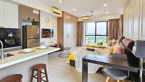 Una habitación de hotel moderna con kitchenette, una cama con colcha colorida, un escritorio con silla y un amplio ventanal con vistas.