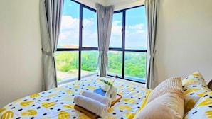 Un dormitorio con un ventanal grande, una cama con colcha estampada y vistas al verdor exterior.