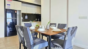Un comedor moderno con una mesa y sillas de madera, un refrigerador y una cocina al fondo.