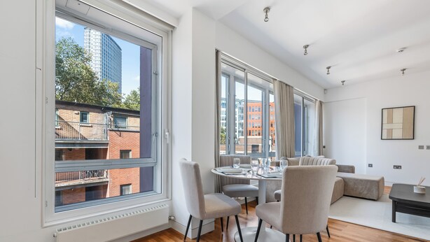 Un espace de salle à manger moderne, avec une table ronde, des chaises et une vue sur la ville grâce à de grandes fenêtres.