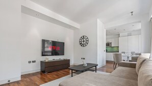 Un salon moderne avec un téléviseur à écran plat, un canapé, une table basse et une cuisine en arrière-plan.