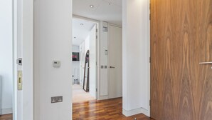 Un couloir avec un plancher en bois, des murs blancs et une porte en bois. On y trouve des prises électriques et un thermostat fixés au mur.