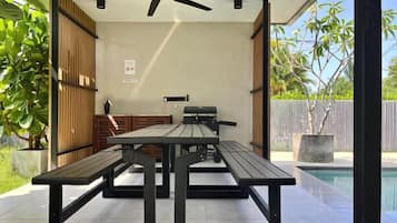 An outdoor patio with a table and benches, a ceiling fan, and a view of a swimming pool.