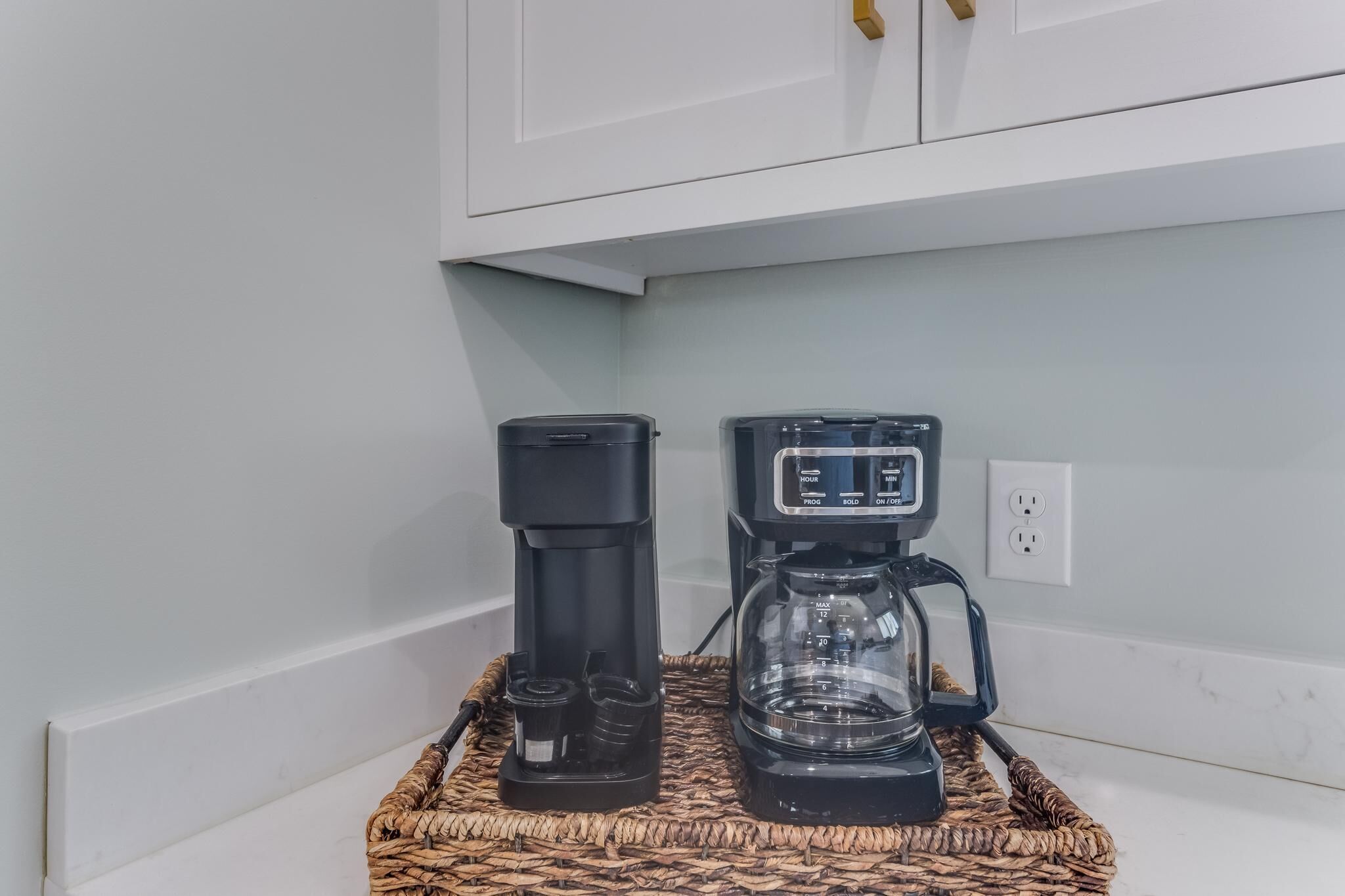 Een keukenhoek met een koffiezetapparaat en een waterdispenser op een geweven dienblad.