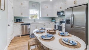 A modern kitchen with white cabinets, stainless steel appliances, and a central island with blue napkins and decorative bowls. - Beautiful New Home Near Beach with Pool Sleeps 6 (Pass Christian)