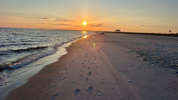 A beach at sunset with footprints in the sand and a structure in the distance. - Beautiful New Home Near Beach with Pool Sleeps 6 (Pass Christian)