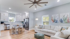 A modern kitchen with white cabinets, a dining table with chairs, a ceiling fan, and artwork on the walls. - Beautiful New Home Near Beach with Pool Sleeps 6 (Pass Christian)