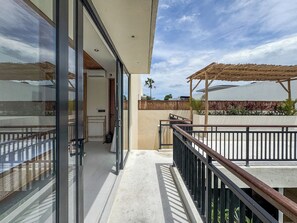 A modern outdoor balcony with a glass door leading to a room, a wooden pergola, and a view of a building in the background. - Athaya Canggu Villas by Nagisa Bali (Canggu)