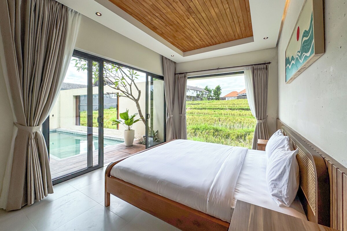 A bedroom with a large bed, a view of a rice field, and a wooden ceiling.