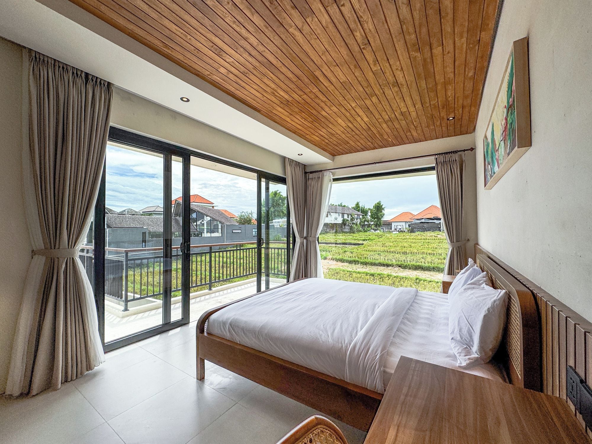 A bedroom with a large bed, wooden ceiling, and a view of a green landscape through large windows.