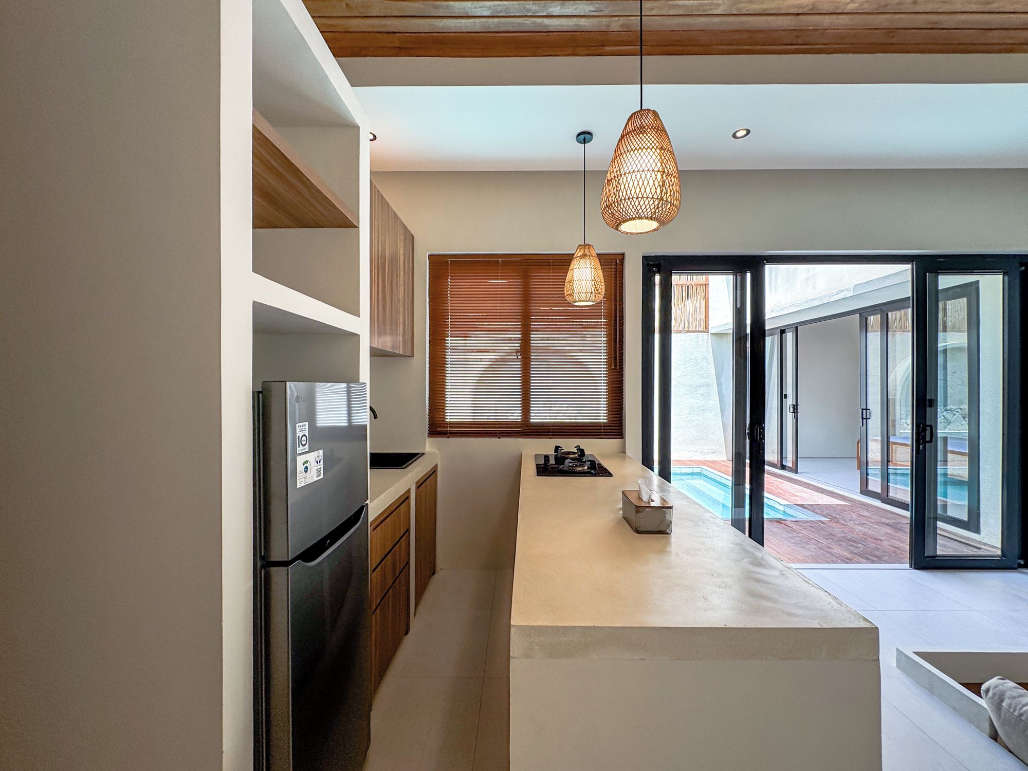 Una cocina moderna con refrigerador empotrado, armarios de madera, una isla central y un amplio ventanal corredera que da a una zona de piscina.