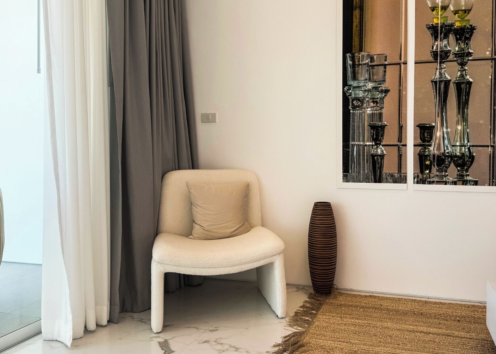 A corner with a white chair, a tall vase, and a window with decorative items.