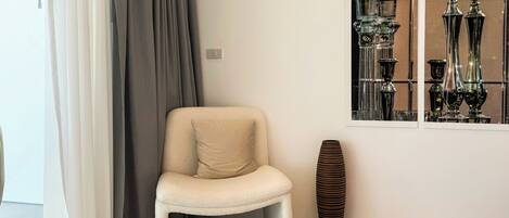 A corner with a white chair, a tall vase, and a window with decorative items.
