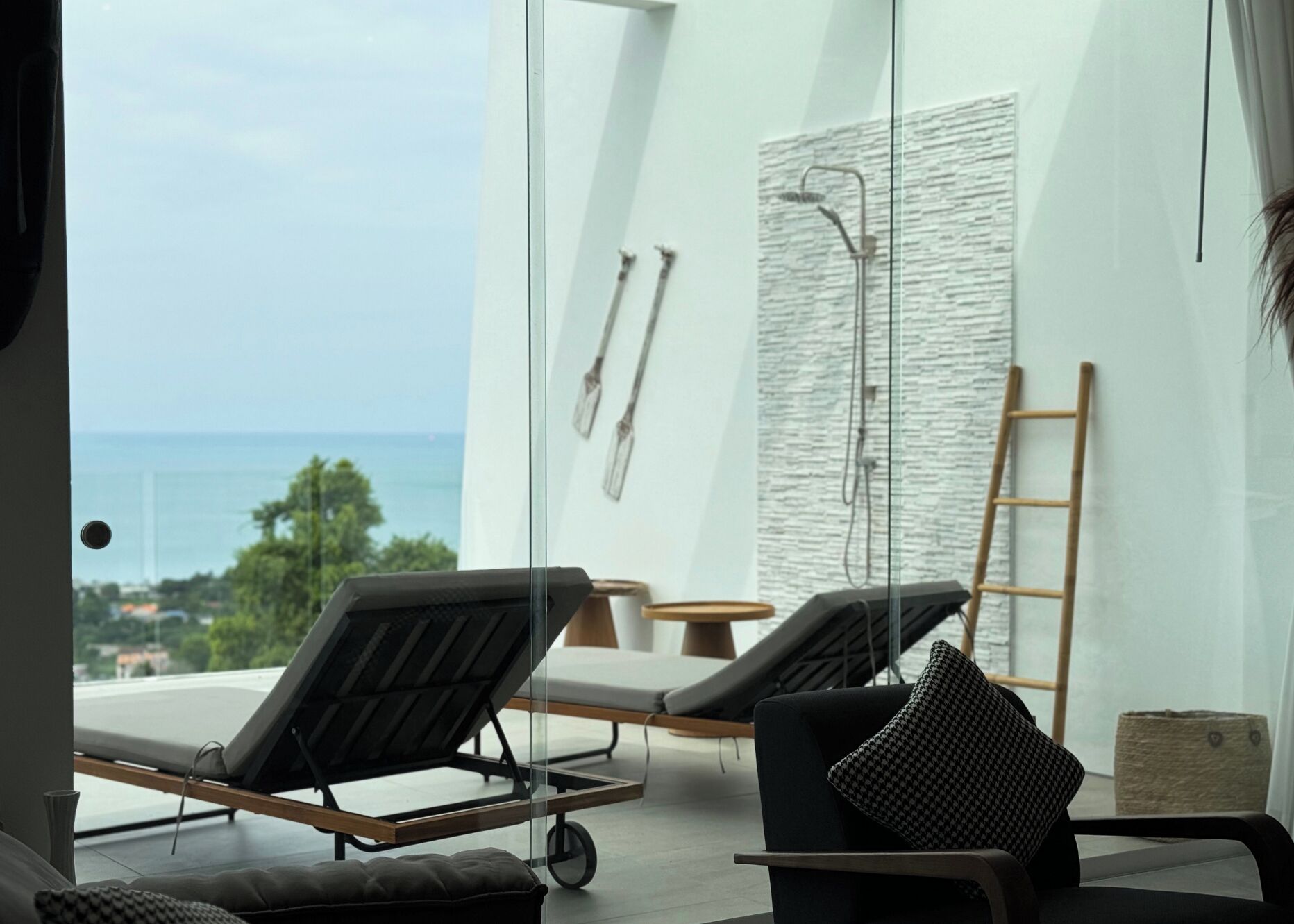 A modern room with a view of the sea, two lounge chairs, a wooden ladder, and a textured wall.