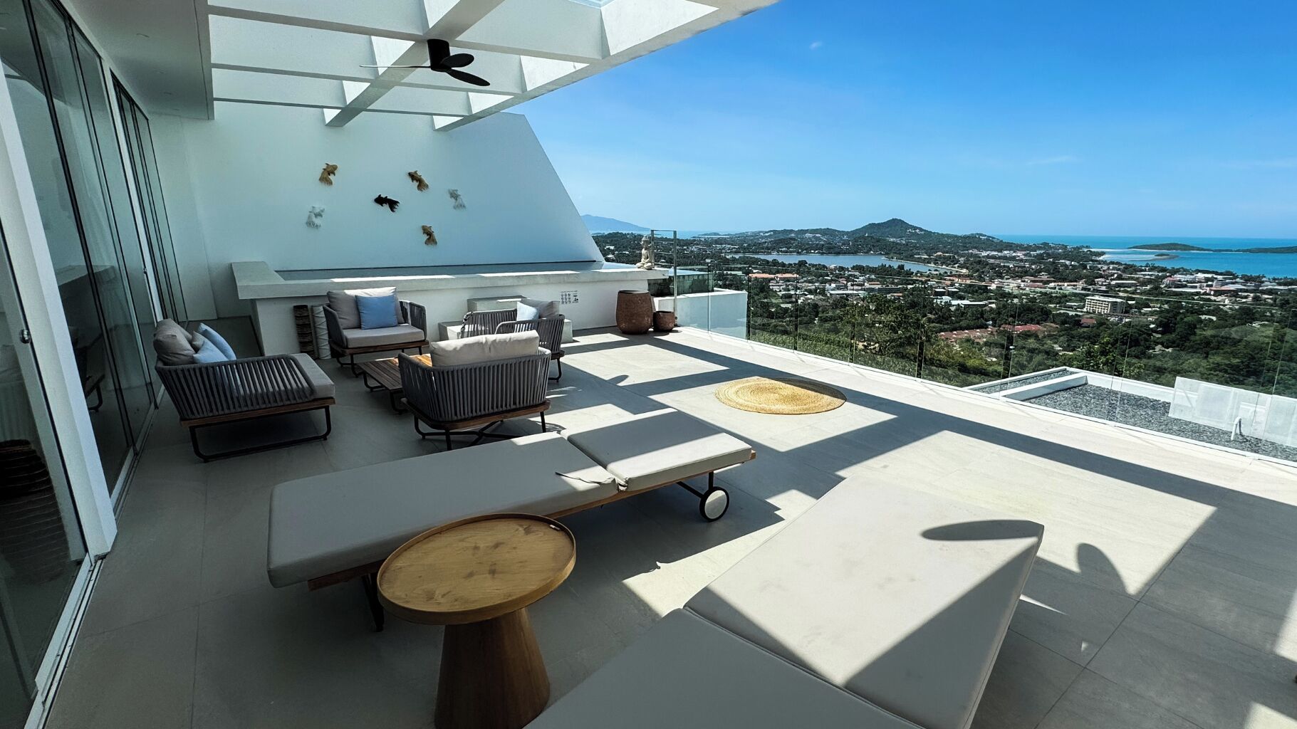 A rooftop terrace with outdoor seating, a ceiling fan, and a panoramic view of a coastal cityscape.