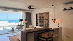 A modern hotel room with a balcony, a desk, a chair, and a large window with a view of the ocean. - Golden Lotus Villas (Koh Samui)